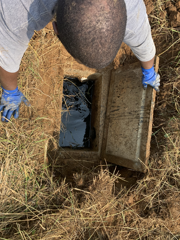 A person inspecting a septic tank distribution box with a partially removed lid.