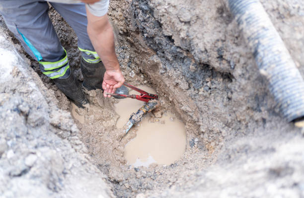 Technician repairing broken sewer line in muddy trench excavation