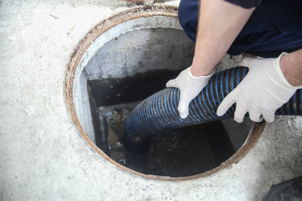Worker inserting hose to clear sewage blockage in access chamber